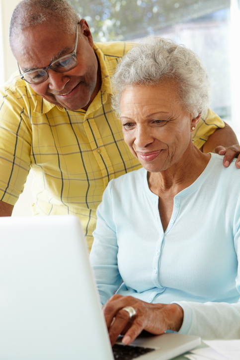 A smiling senior couple using a white laptop at home.
